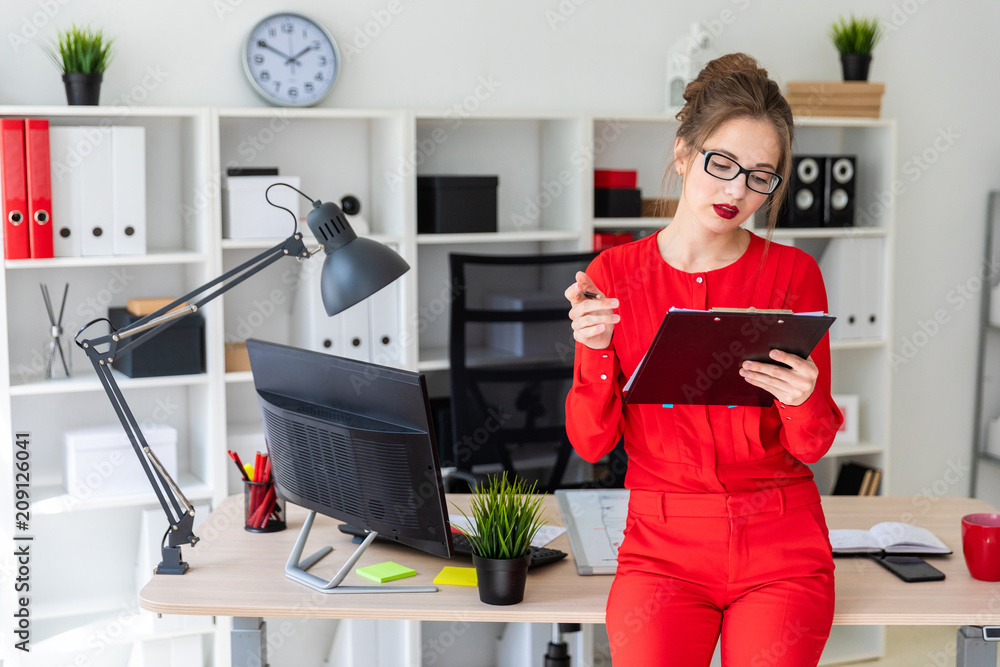 A young girl is standing leaning on a table and is holding a pencil and documents. A young girl is standing leaning on a table and is holding a pencil and documents.