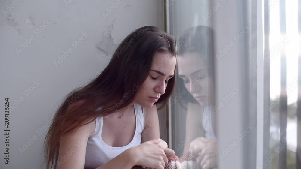 Young sad depressed woman is sitting on the floor and looking out the window. Lonely woman suffering distress in hospital with the suicide thoughts. Young sad depressed woman is sitting on the floor and looking out the window. Lonely woman suffering distress in hospital with the suicide thoughts.
