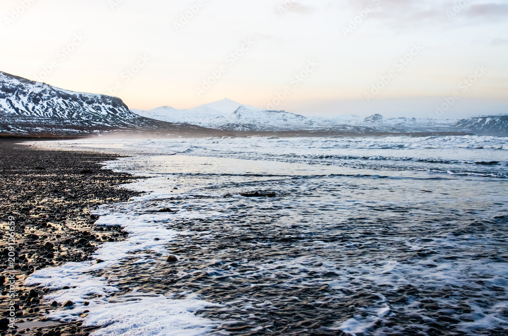 Amazing winter landscape with black beach, ocean and Snæfell volcanic mountain in the background