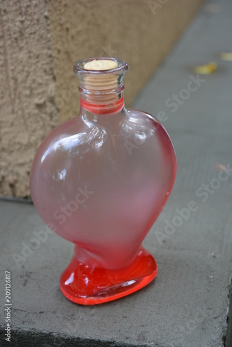 On the background of gray cement is a glass bottle in the form of a heart with a matte red liquid, a very beautiful shape