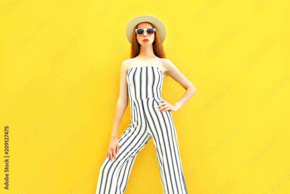 Fashion model woman is wearing a white striped pants, round hat colorful yellow background