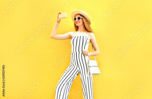 Fashion smiling woman is taking a picture on a smartphone in the city on colorful yellow background