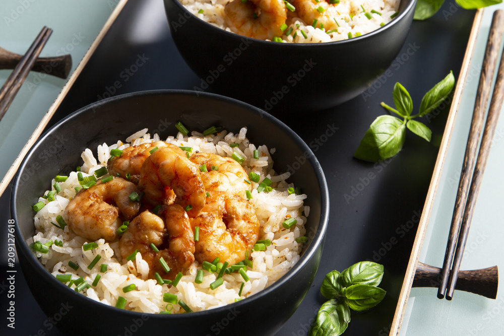 Two bowls of black color with rice and fried shrimp on a blue table. Asian food. Two bowls of black color with rice and fried shrimp on a blue table. Asian food.