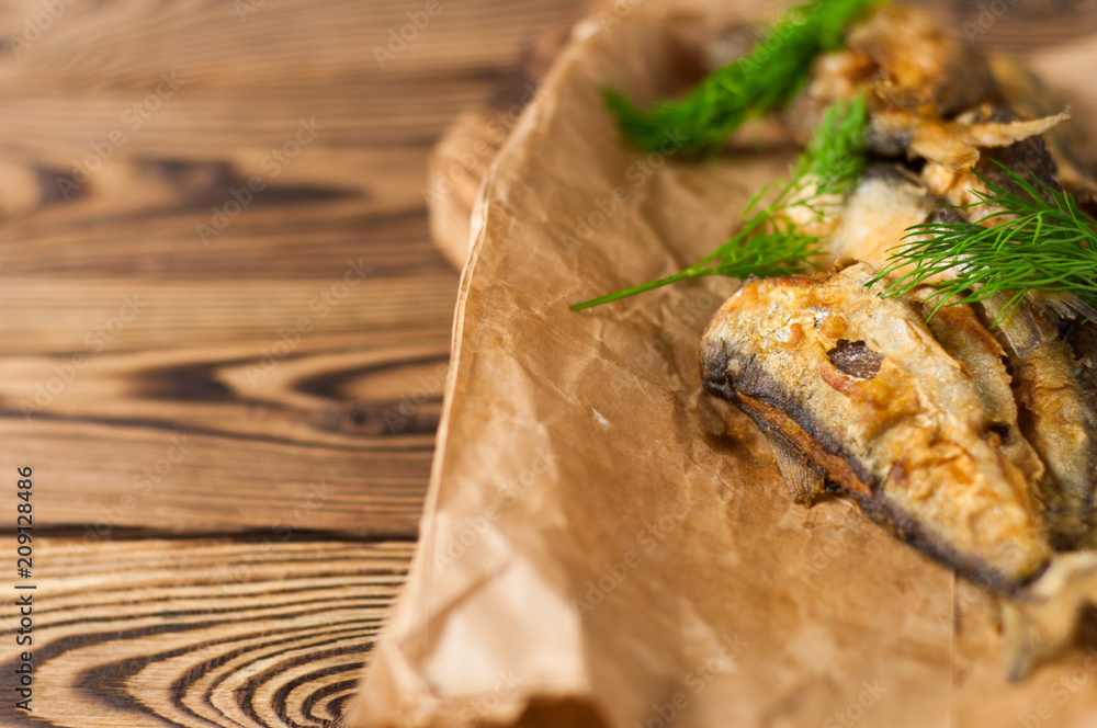 Heap of fried tasty fishes and twigs of fresh green dill on wrinkled paper on cutting board on old wooden rustic brown table with copy space for your text Heap of fried tasty fishes and twigs of fresh green dill on wrinkled paper on cutting board on old wooden rustic brown table with copy space for your text