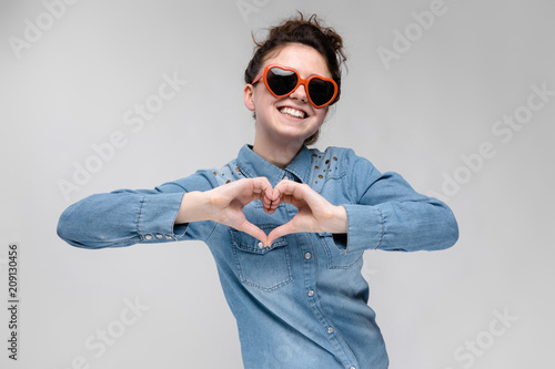 Young brunette girl with glasses in the form of a heart. The hairs are gathered in a bun. The girl folded her heart. photo