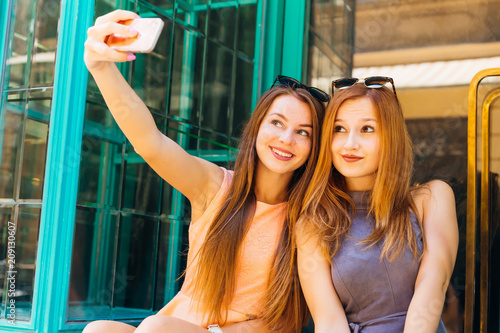 cute girls with sunglasses on their heads make a selfie on the background of glass doors © Ivan