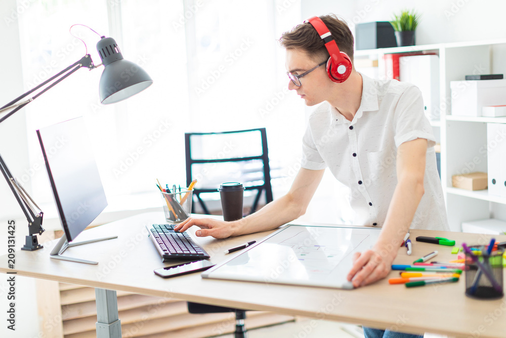 A young man with glasses and headphones is working at the computer. Before the guy is a magnetic board and markers. A young man with glasses and headphones is working at the computer. Before the guy is a magnetic board and markers.