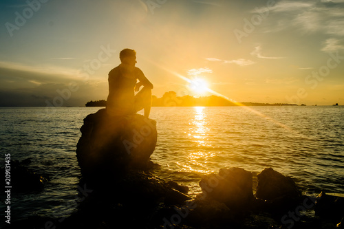 Handsome man sitting on a rock on the beach and watching the sunset, Maldives © matilda553