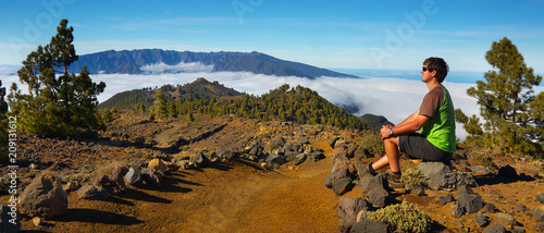 Man sitting on the stone watching a volcanic landscape of pine forest with a Caldera de Taburiente on background, island of La Palma, Canary Islands, Spain