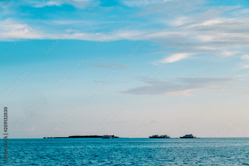 Maldives background. Sunset over the tropical sea and coral beach with colorful clouds in the sky. Boats on the horizon in heavenly atoll of peace and relaxation. Maldives background. Sunset over the tropical sea and coral beach with colorful clouds in the sky. Boats on the horizon in heavenly atoll of peace and relaxation.