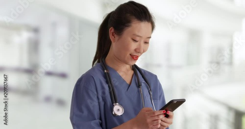 Close up of female millennial nurse dressed in scrubs using smartphone to send text messages indoors hospital, Happy young Asian doctor texting with cell phone inside clinic, 4k