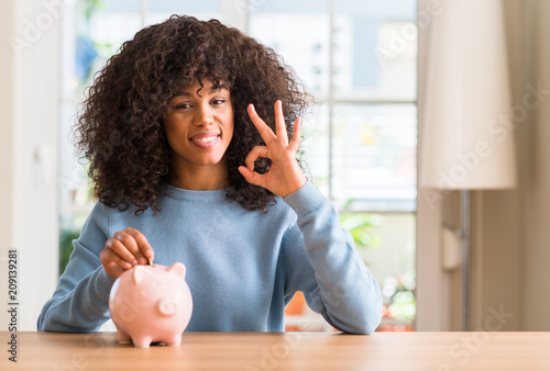 African american woman saves money in piggy bank doing ok sign with fingers, excellent symbol photo