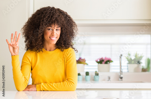 African american woman wearing yellow sweater at kitchen showing and pointing up with fingers number four while smiling confident and happy.