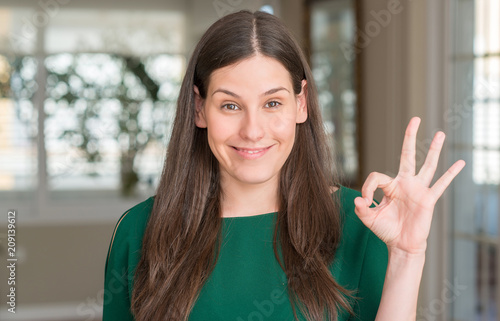 Young beautiful woman at home doing ok sign with fingers, excellent symbol