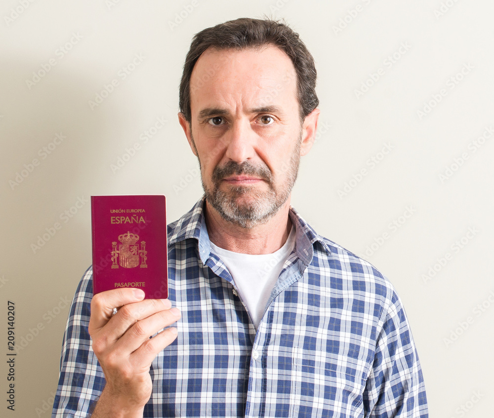 Senior man holding spanish passport with a confident expression on smart face thinking serious Senior man holding spanish passport with a confident expression on smart face thinking serious