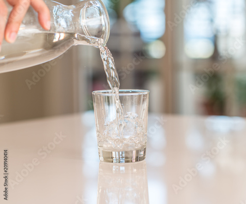 Closeup of bottle pouring watter in a glass on the table with sunny bokeh background at home.