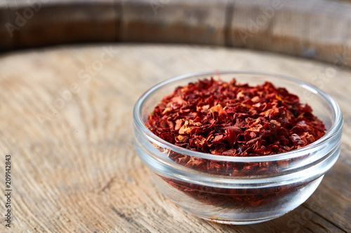 Transparent glass bowl with dried chilly on wooden barrel background, close-up, shallow depth of field.