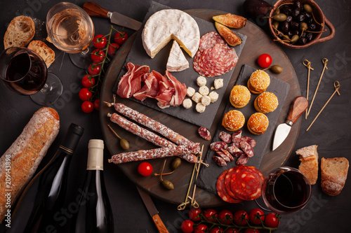 Appetizers table with differents antipasti, cheese, charcuterie, snacks and wine. Mini burgers, sausage, ham, tapas, olives, cheese and baguette over grey concrete background. Top view, flat lay