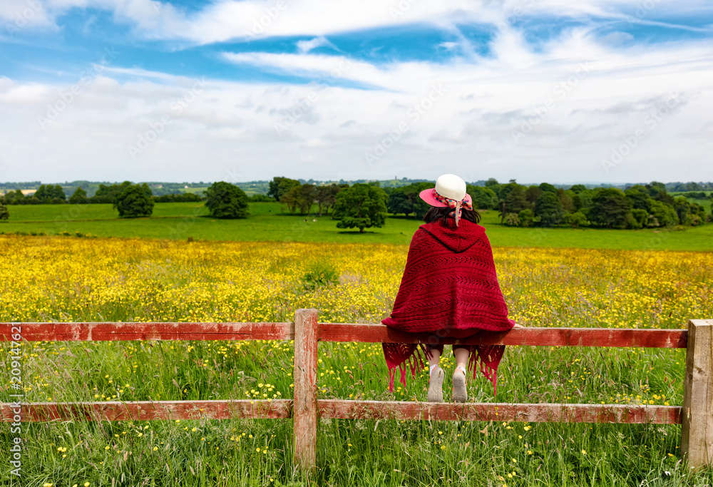 Woman looking into field while sitting on fence