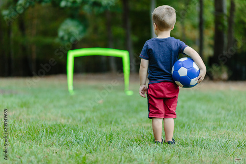 Young boy looking towards a practice goal with a soccer ball under his arm photo