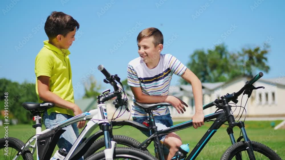 Two little boys with bicycles on the nature communicate with each other, smile. Slow motion, middle shot