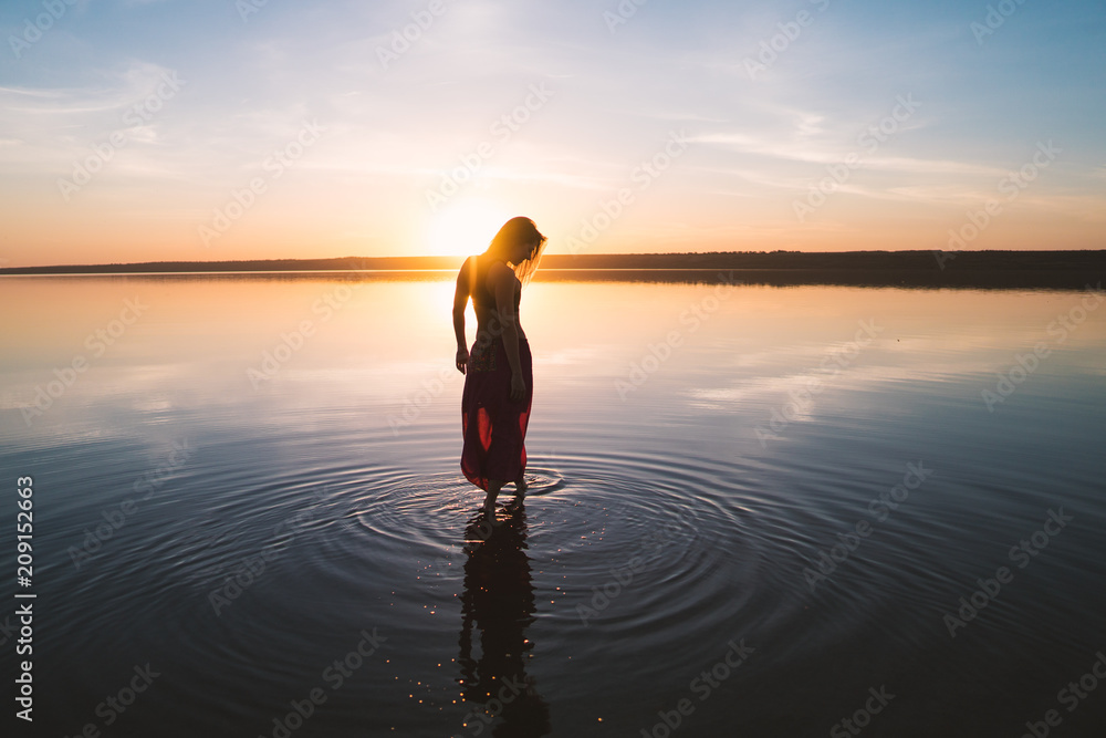 Silhouette woman on the beach at sunset . She stands in water. Morning natural stretch warm-up training Silhouette woman on the beach at sunset . She stands in water. Morning natural stretch warm-up training