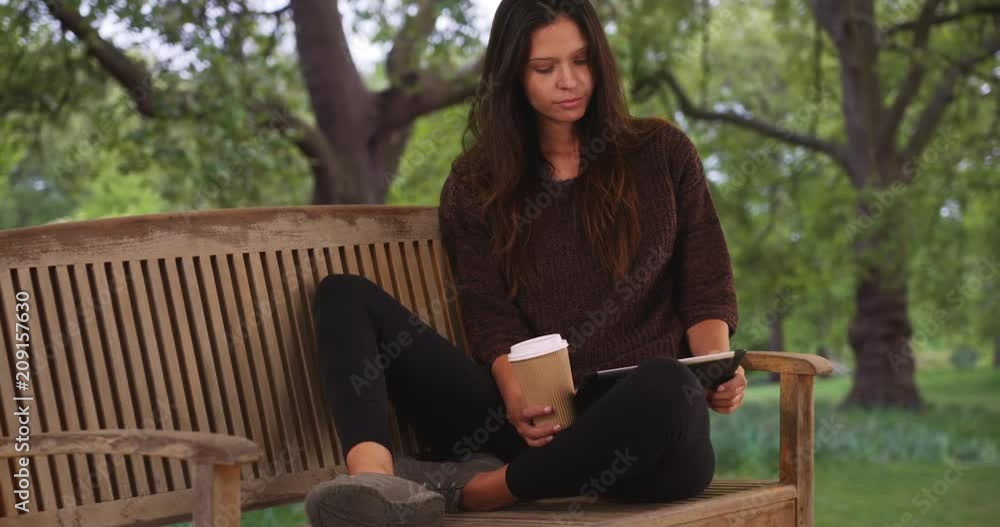 Millennial woman sitting on park bench using tablet computer and drinking coffee while visiting London, Tourist sipping drink and using device to plan vacation, 4k Millennial woman sitting on park bench using tablet computer and drinking coffee while visiting London, Tourist sipping drink and using device to plan vacation, 4k