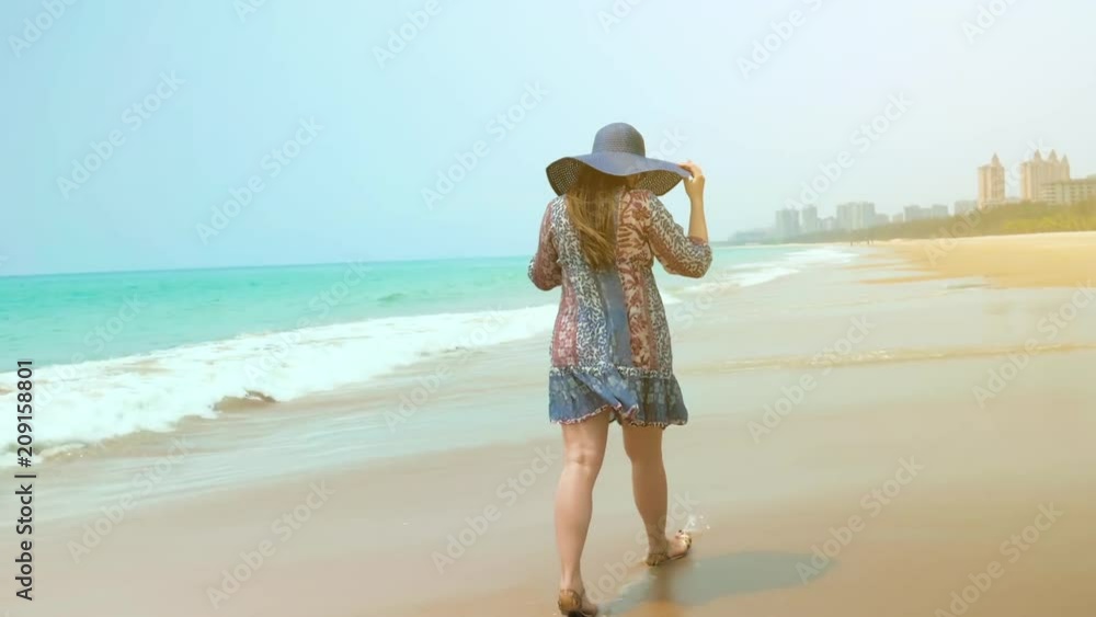 Beautiful happy girl in blue hat walks on beach on sunny summer day against a blue sky. Medium Shot. Beautiful happy girl in blue hat walks on beach on sunny summer day against a blue sky. Medium Shot.