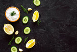 Greek yogurt dip with greenery, cucumber, oranges, garlic on black background top view pattern copy space