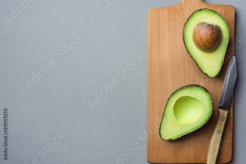 Ripe Evenly Halved Organic Australian Avocado with Pit on Wooden Cutting Board with Knife Grey Background. Healthy Lifestyle Vegan Vitamin E Oil. Creative Minimalist Food Poster Banner Copy Space