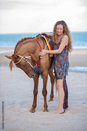 Happy smiling attractive blond wavy hair woman riding a horse on the Beach, relaxing time concept. © May_Chanikran