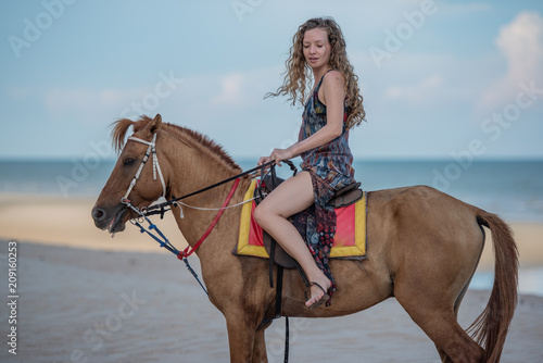 Happy smiling attractive blond wavy hair woman riding a horse on the Beach, relaxing time concept.