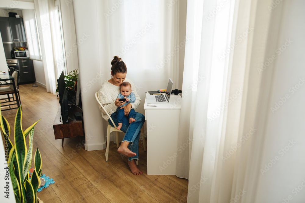 Young woman working with her baby at home. Young woman working with her baby at home.