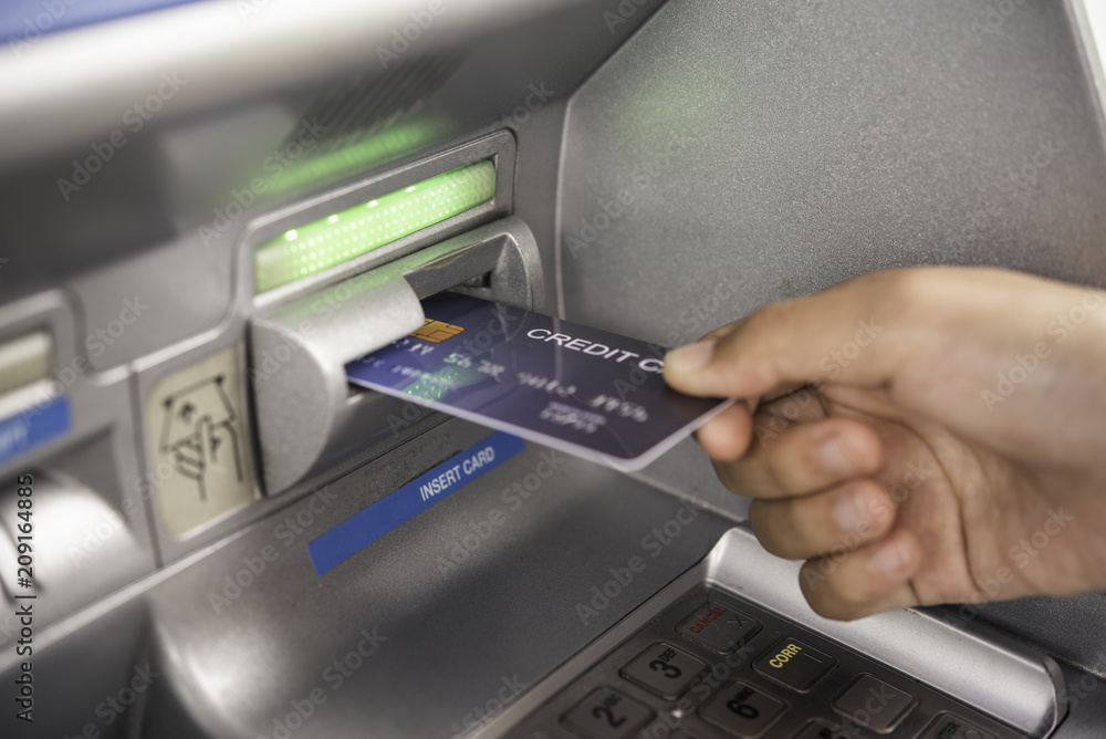 Hand inserting with a credit card into bank machine . Man using an atm machine with credit card to withdraw money Hand inserting with a credit card into bank machine . Man using an atm machine with credit card to withdraw money