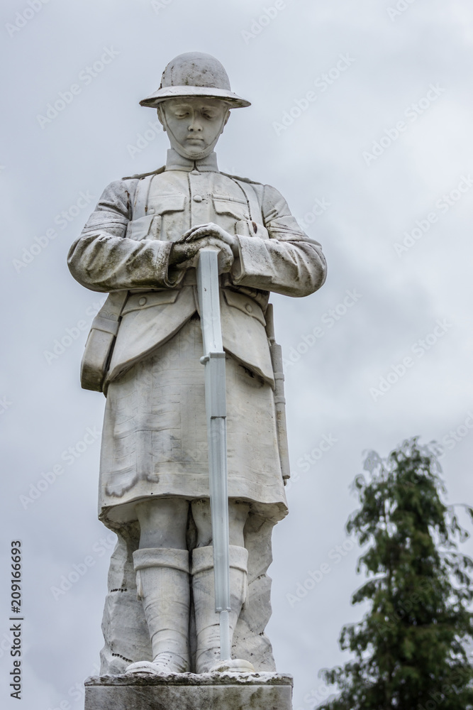 Naklejka premium Fort William, Scotland - June 11, 2012: Closeup of white stone war memorial statue on The Parade against gray sky. Shows young soldier in kilt contemplating.