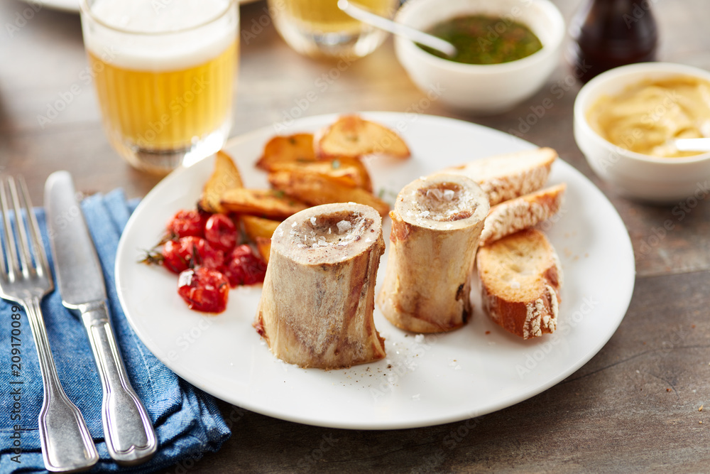 Marrow bones served on plate with toasts, potato and tomatoes. Marrow bones served on plate with toasts, potato and tomatoes.