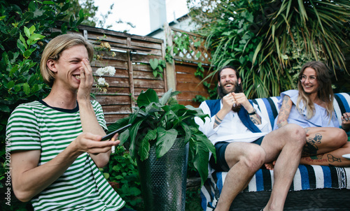 A young man realises his mistake while two friends look at him and smile photo