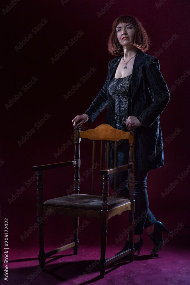 Confident ugly woman wearing black suit siting and posing in front of camera on stage with crimson floor Confident ugly woman wearing black suit siting and posing in front of camera on stage with crimson floor