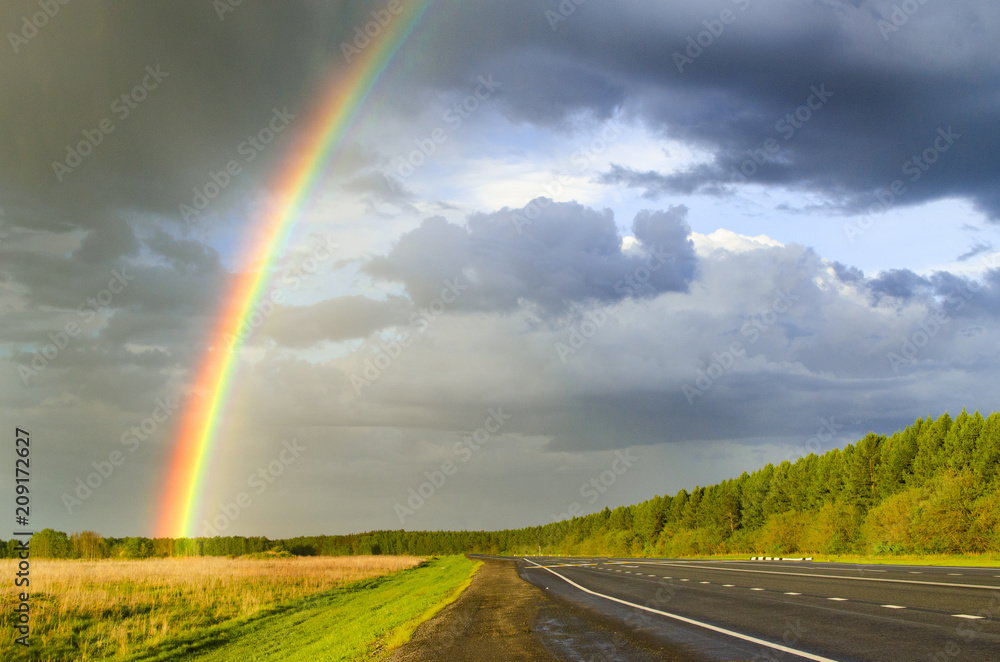 wet highway after rain with a rainbow against the backdrop of a rainy sky