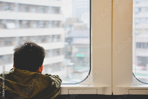 back side of little boy traveling by train and looking out through glass window, child problem or travel concept, vintage effect