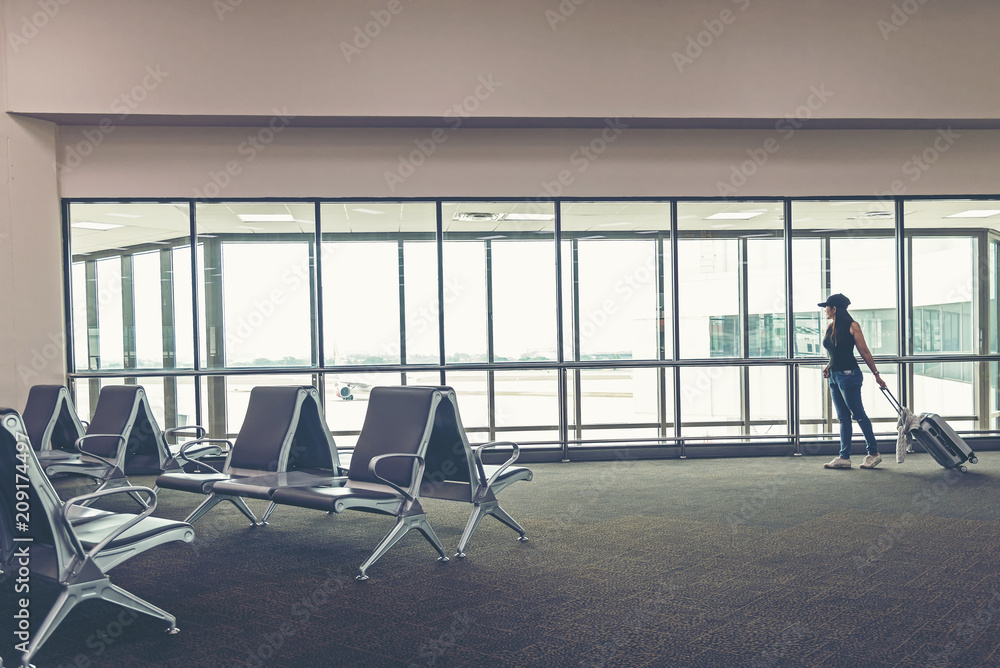 Fototapeta premium Traveler woman plan and backpack see the airplane at the airport glass window, girl tourist hold bag and waiting near luggage in hall airplane departure. Travel Concept .