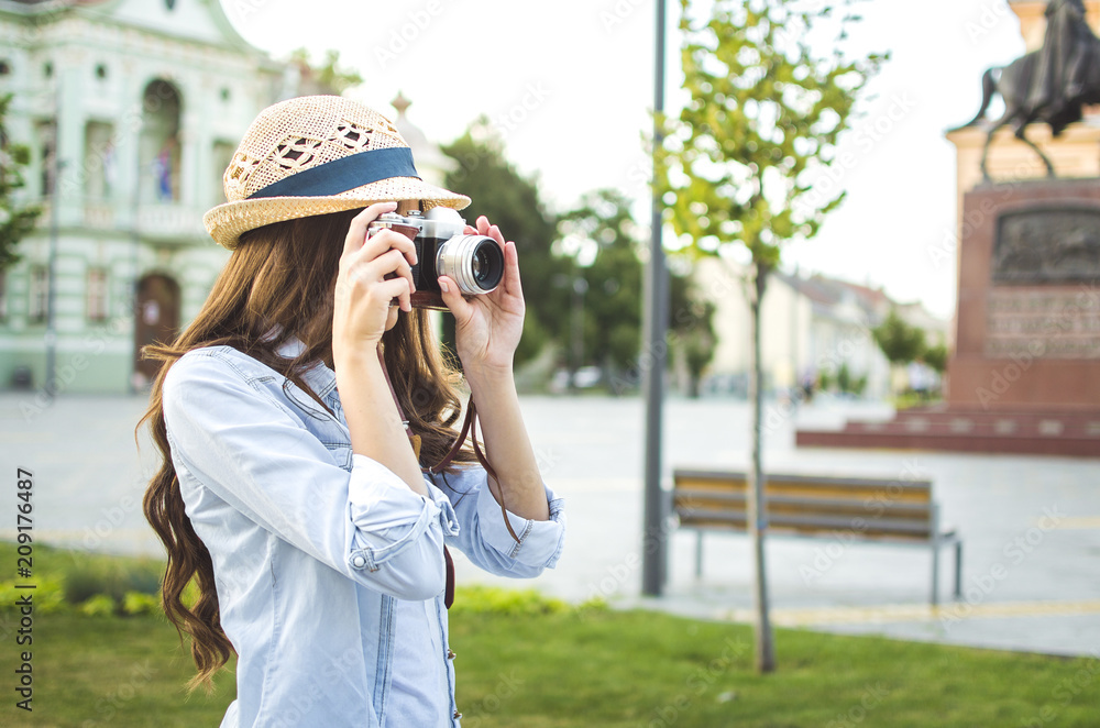 Pretty girl wearing hat taking picture with an old retro camera in the city in Europe