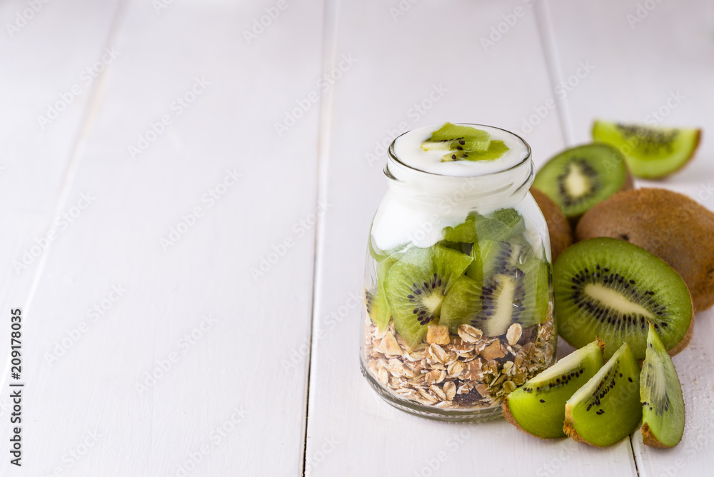 White yogurt with muesli in glass bowl with pieces of kiwi on top and whole pieces on the right side. White yogurt with muesli in glass bowl with pieces of kiwi on top and whole pieces on the right side.