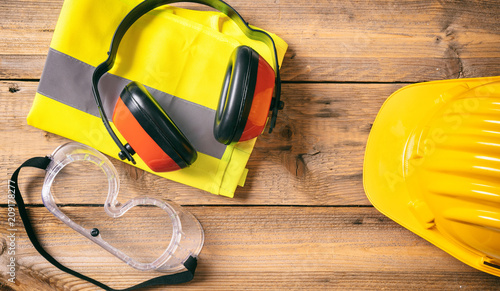 Construction safety. Protective hard hat, headphones and glasses on wooden background, copy space, top view