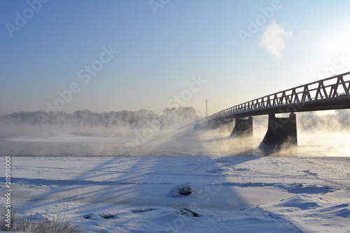 Winter day. Landscape with bridge over the river, that does not freeze and above it rises the steam.
