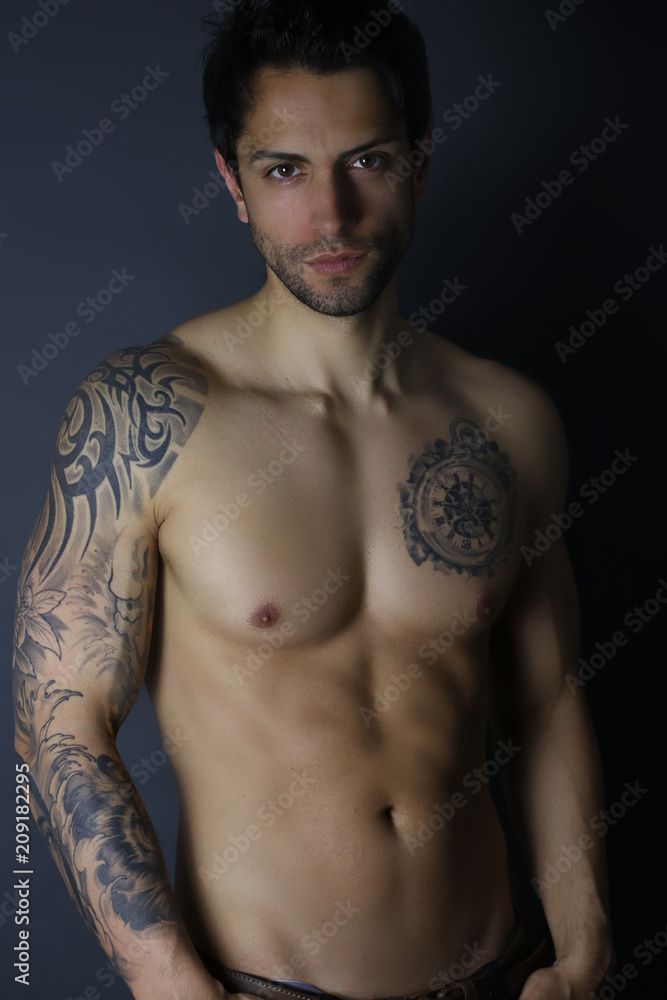 Sexy male model posing shirtless on gray background . Handsome tattooed man Sexy male model posing shirtless on gray background . Handsome tattooed man