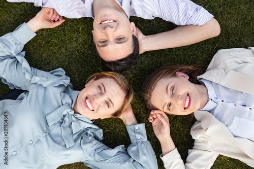 Happy employers. Three smiling happy employers feeling relaxed while lying on the grass outside the office