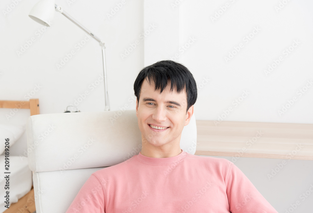 Portrait of a satisfied man relaxing with the arms in the head sitting on a chair at home with a warm light from a window. young man indoors with very handsome face in pink casual shirt Portrait of a satisfied man relaxing with the arms in the head sitting on a chair at home with a warm light from a window. young man indoors with very handsome face in pink casual shirt