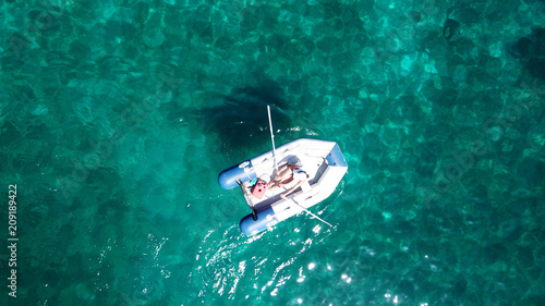 Aerial bird's eye view of small inflatable rib boat operated by young woman in turquoise clear water sea