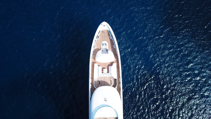 Aerial drone bird's eye top view photo of luxury yacht with wooden deck docked in deep blue waters of Mykonos island, Cyclades, Greece